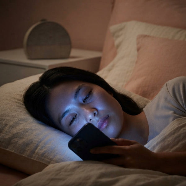 A person lying in bed at night lit by the harsh blue light of a smartphone screen in a dark bedroom.